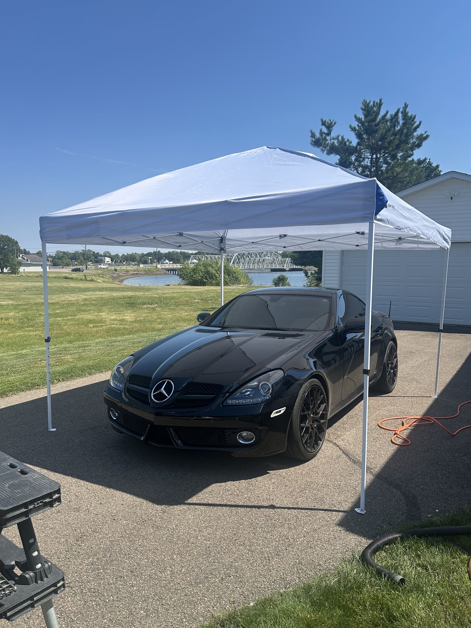 Mobile detailing setup with a canopy tent over a car being detailed in a driveway