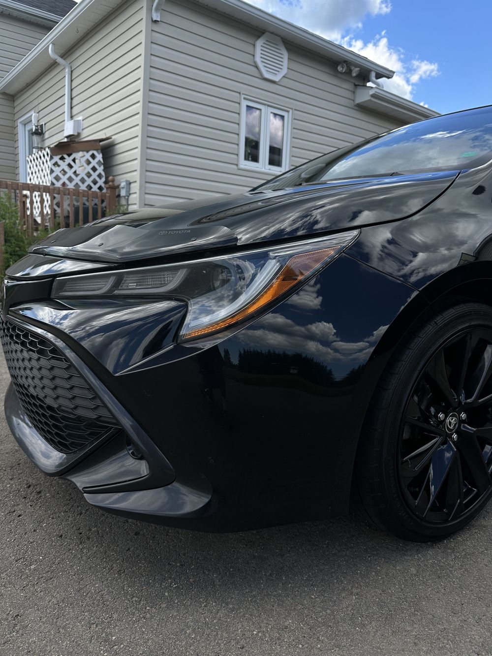Close-up of a black Toyota's hood and headlight showing deep, glossy paint reflection after enhancement